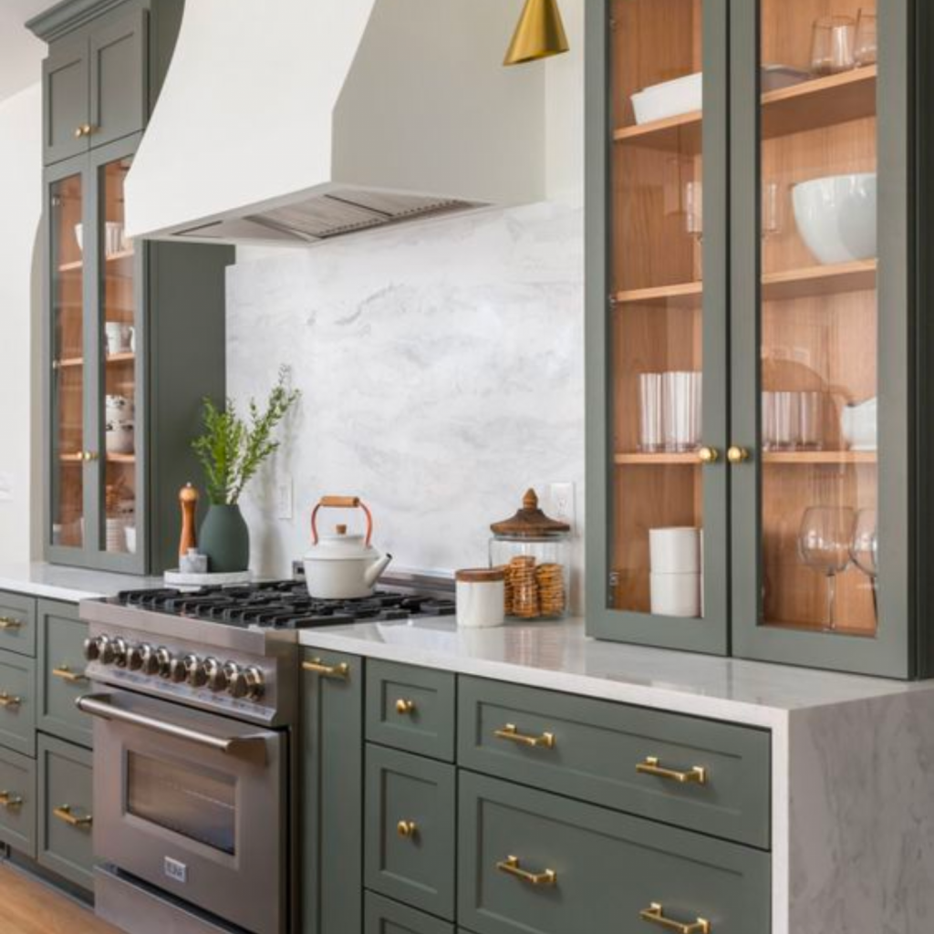 Kitchen design at a showroom with green cabinetry, glass upper cabinets and a white custom hood. 