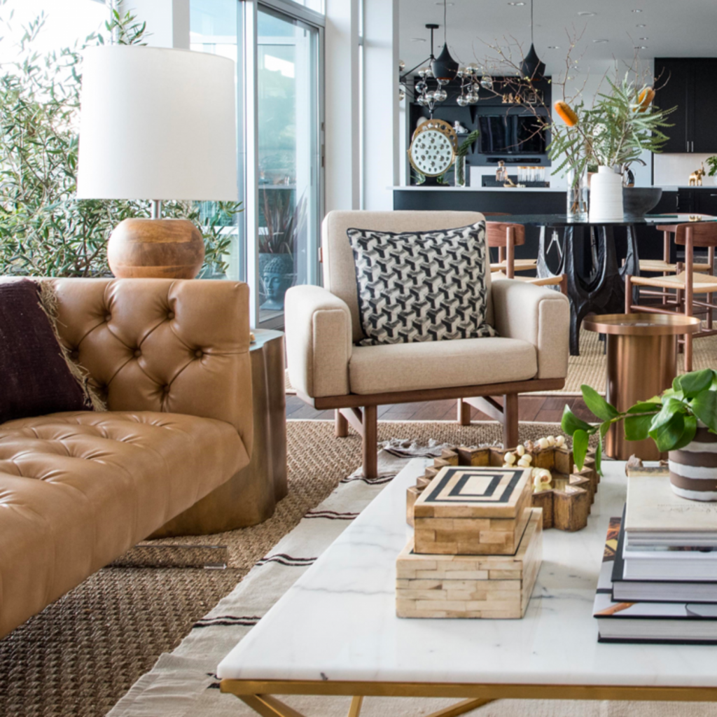 Mid-century modern design living room with an open plan into the black kitchen.  Leather, tufted sofa is paired with a brass and marble top coffee table and a nude wooden armchair.  