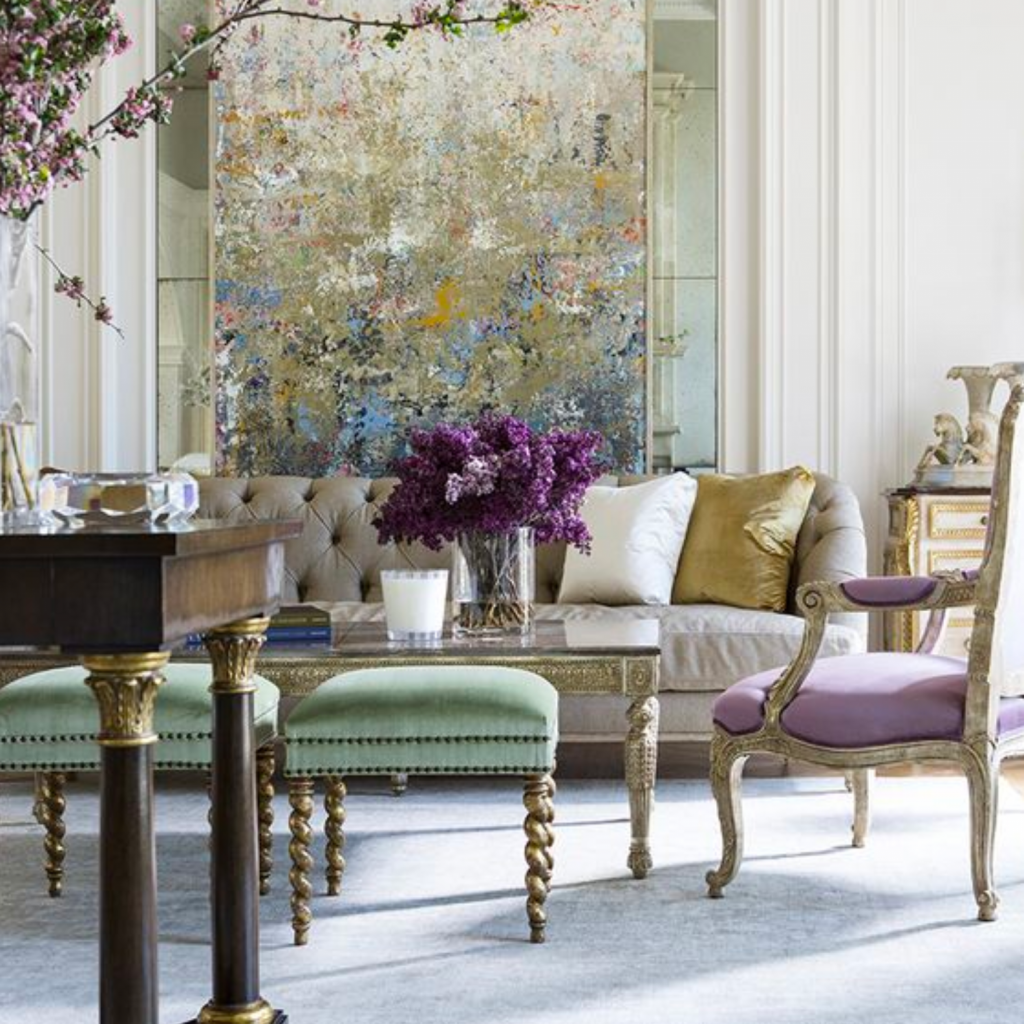 Traditional interior design style living room with a classic, nude, tufted sofa.  An ornate, glass coffee table is flanked by two purple classic armchairs.  Opposite the sofa are to green ottomans.